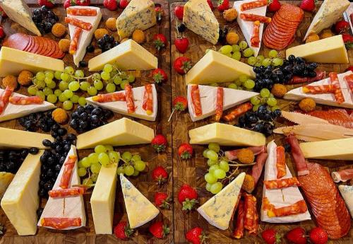 Assorted cheeses presented on large teak chopping boards with cured meats, grapes and strawberries.