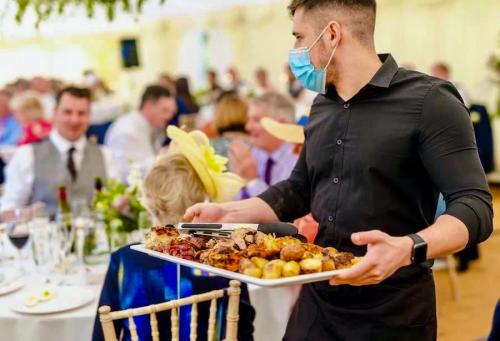 Waiter carrying a platter of the wedding ‘s main course menu, showing wedding guests in the background.