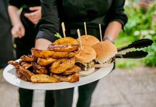 Sharing platter of Cajun potato wedges, proper cheeseburgers and Jamaican jerk chicken being offered by a waitress.