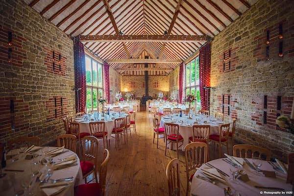 Inside Bartholomew Barn, a wedding venue in Kirdford, West Sussex with tables set up ready for a wedding reception